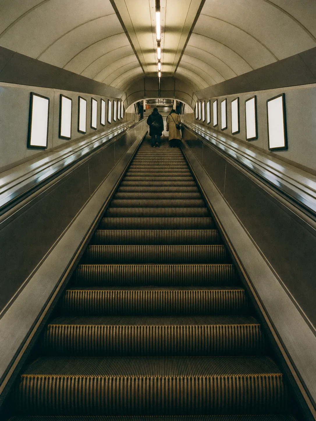 Looking up a London Underground escalator shaft at night, the treads and lit panels receding towards the top.